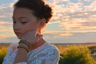 Thoughtful girl against cloudy sky during sunset