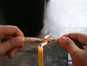 Close-up of hand holding rope over burning candle