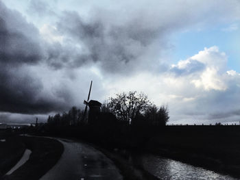 Road passing through field against cloudy sky