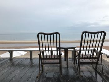 Empty chairs by sea against sky