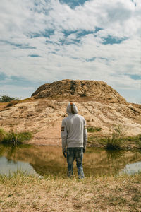 A man standing infront of water looking at a big rock object