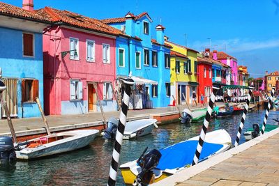 Boats moored in canal by houses against sky in city