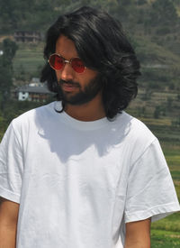 Portrait of a handsome long haired indian young men wearing sunglasses with with standing outside 