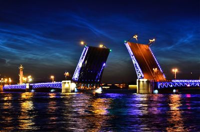 Illuminated city by river against sky at night