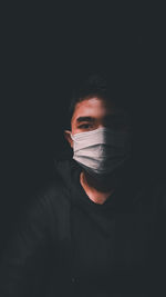 Close-up portrait of young man wearing mask against black background