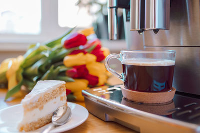 Cup of coffee with milk, piece of cake and tulips flowers on wooden kitchen table. freshly brewed 