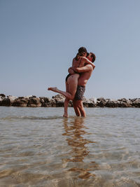 Full length of shirtless man standing in sea against clear sky