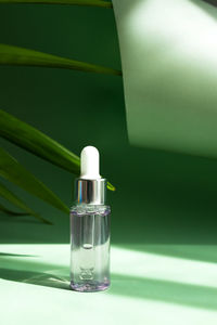 Transparent cosmetic bottle with a pipette in the rays of the bright sun on a green background