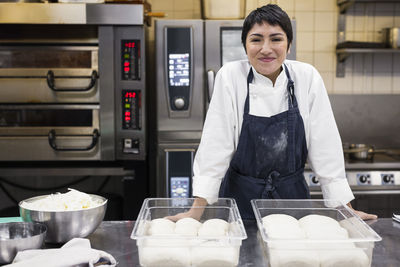 Portrait of smiling female chef with dough in commercial kitchen