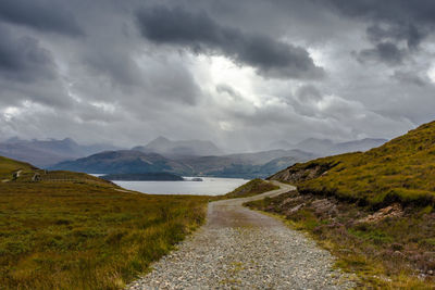 Pathway leading towards lake by mountains against sky