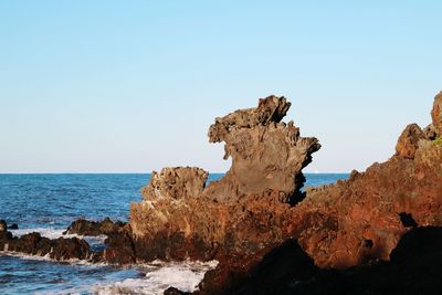 Rock formation by sea against clear blue sky