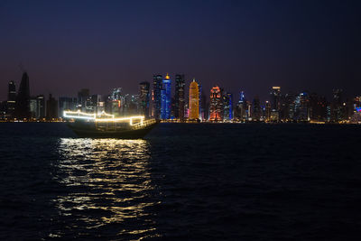 Illuminated buildings by sea against sky at night