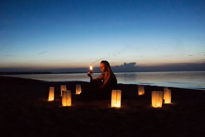 Woman sitting amidst lanterns at beach during dusk