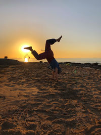 Full length of man jumping on beach against sky during sunset