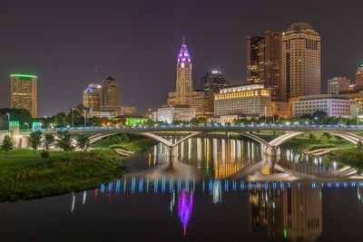 Illuminated buildings by river against sky in city at night