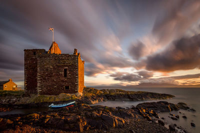 Old building by sea against sky during sunset