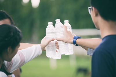 Cropped image of friends toasting water bottles while standing in park