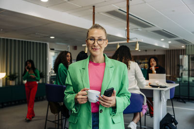 Portrait of smiling mature businesswoman holding coffee cup at office