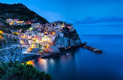 Aerial view of illuminated city by sea against sky