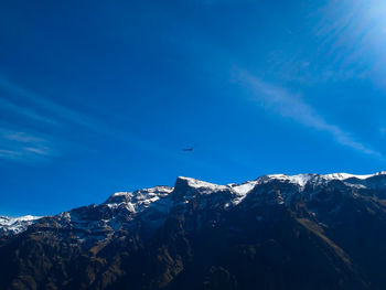 Low angle view of birds flying over snowcapped mountains against blue sky