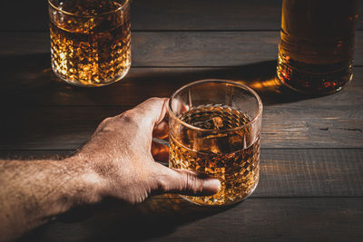 Hand holding whisky glass with ice on wooden table background. close up.