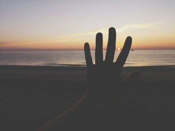 Silhouette hand by sea against sky during sunset