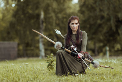 Full length of woman holding bow and arrow crouching on grass
