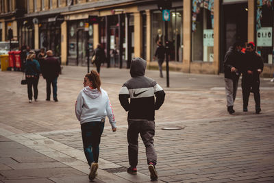 Rear view of people walking on sidewalk in city