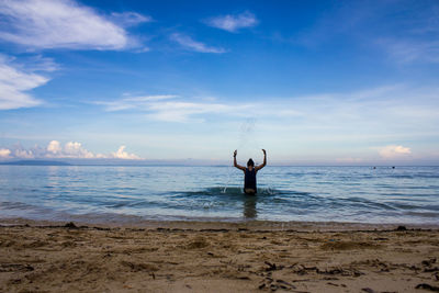 Rear view of woman splashing water in sea against sky