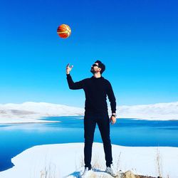 Full length of young man playing with basketball against lake during winter