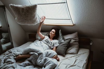 Young woman throwing a pillow out of bed at home