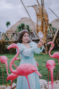 Smiling young woman wearing dress and crown looking in mirror while standing outdoors