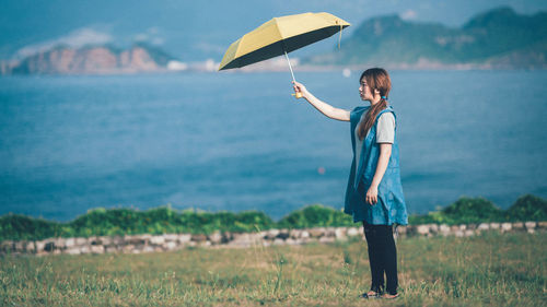 Side view of young woman holding umbrella while standing by lake