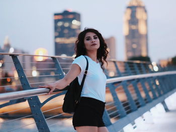 Young woman standing on railing in city against sky