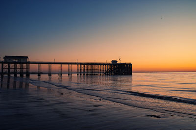 Pier on sea against clear sky during sunset