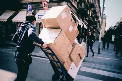 Man pushing cart with cardboard boxes on street in city