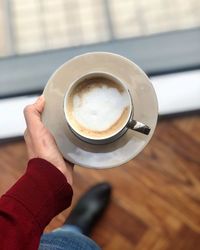 Close-up of hand holding coffee cup on floor 