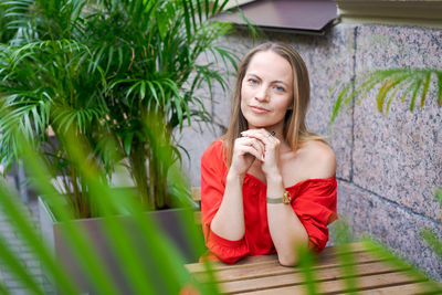 A confident young woman sits at a table in a street cafe in a red dress