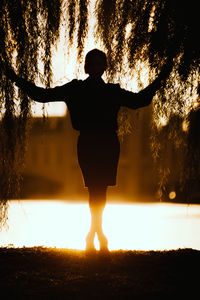 Silhouette woman standing under tree on field during sunset