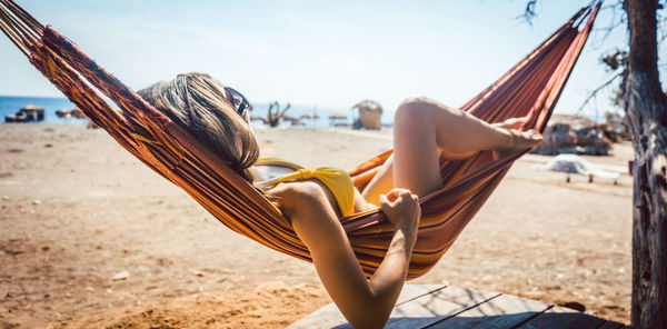 Woman lying on hammock at beach during sunny day