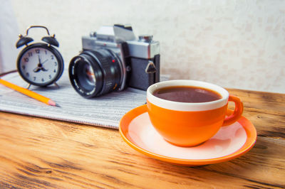 Close-up of coffee cup with camera and alarm clock on table