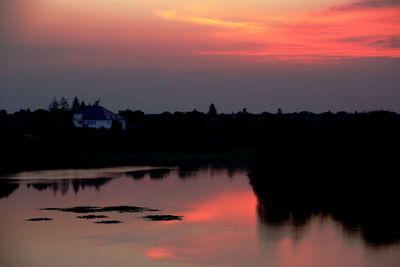 Silhouette trees by lake against romantic sky at sunset