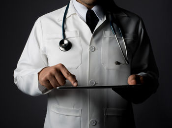 Midsection of doctor holding digital tablet over black background