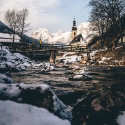 Frozen river by buildings against sky during winter