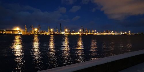 Panoramic view of illuminated factory by sea against sky at night