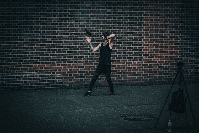 Full length of man juggling bottles against brick wall