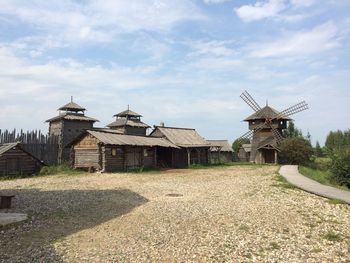 Traditional windmill on field by building against sky