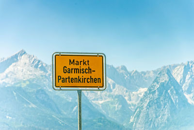 Warning sign on snowcapped mountain against sky