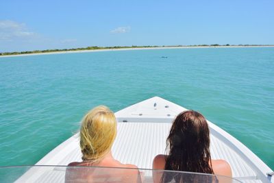 Rear view of women sitting in boat on sea against blue sky