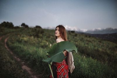 Portrait of woman holding leaf while standing on grassy land